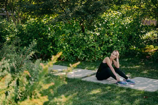 Horizontal full length shot of pleased brunette sporty woman listens motivation playlist before start running dressed in active wear poses on path uses application online. Sport and wellness concept photo