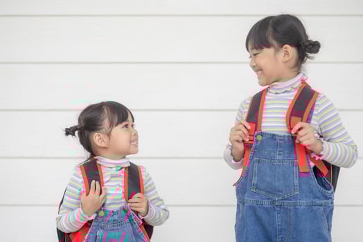 Back to school. Two cute Asian child girls with school bags holding a book together on white background photo