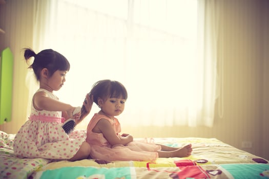 Lovely little girl brushing hair of her sister while sitting on the bed photo