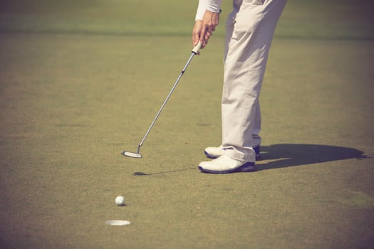 Golf player at the putting green hitting ball into a hole photo