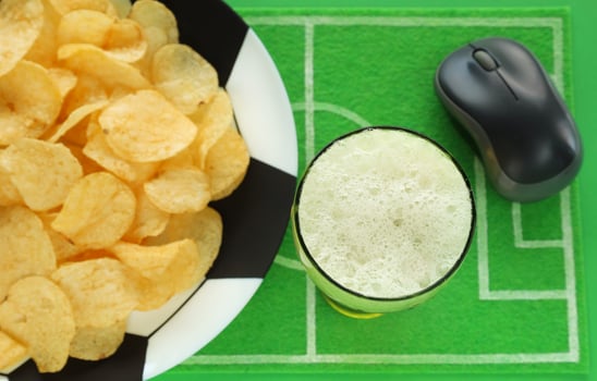 Football soccer party table with snacks and beverage. Potato chips on big plate painted like soccer ball, glass of beer, on dish mat, top view. Computer mouse for watching match broadcast online. photo