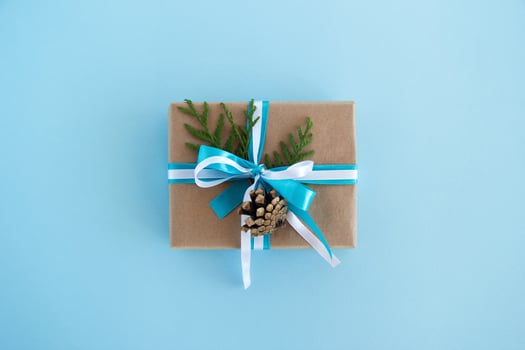 Gift box wrapped of craft paper, blue and white ribbons and decorated fir branches and pinecone on the blue background, top view. Christmas present. photo