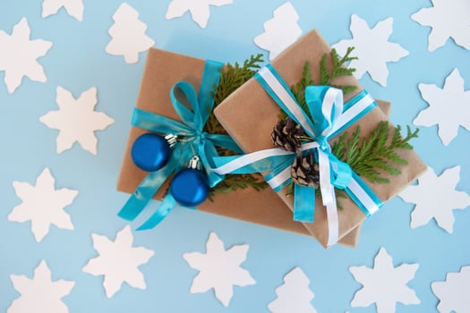 Two gift boxes wrapped of craft paper, blue and white ribbon and decorated fir branches, blue Christmas balls and pinecones on the blue background with white paper fir tree and star, top view. photo