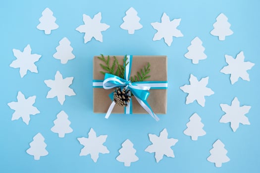 Gift box wrapped of craft paper, blue and white ribbons and decorated fir branches and pinecone on the blue background with paper white fir tree and star, top view. Christmas present. photo