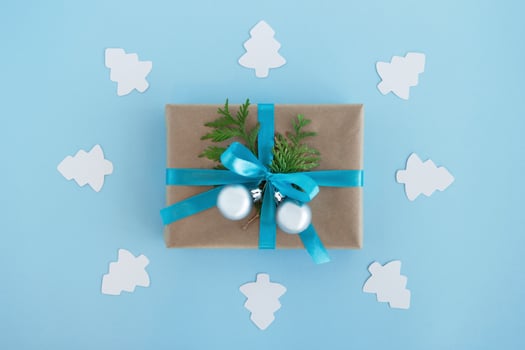 Gift box wrapped of craft paper, blue ribbon and decorated fir branches and silver Christmas balls with white paper fir tree around on the blue background, top view. Christmas present. photo