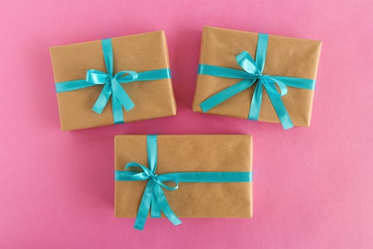 Three gift boxes wrapped of craft paper and blue ribbon on the pink background, top view. photo