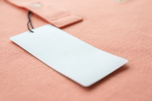 Blank white clothes tag label on pink fabric texture background photo