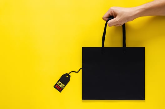 Hand holding a black shopping paper bag with black price tags on yellow background for Black Friday shopping sale concept. photo