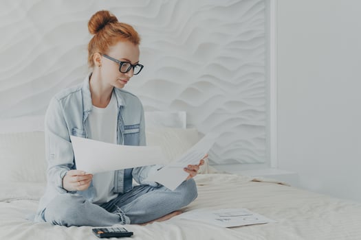 Young concentrated woman housewife in spectacles managing family budget while sitting on bed at home photo