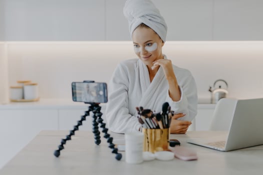 Blogging modern technologies skin care and beauty concept. Pleased beautiful woman records video tutorial at home applies beauty pads under eyes shoots broadcast live video to social network photo