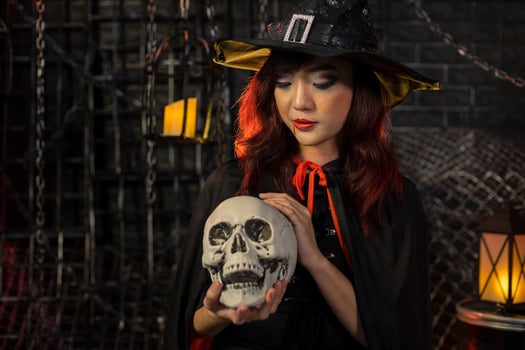 Asian girl in witch costume holding human skull for halloween party trick or treat concept with dark black background with copy space photo
