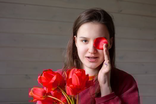 portrait of a brown-haired woman with a bouquet of red tulips on a gray wooden background. a girl in a red pullover with long hair holds a bouquet of tulips in her hands and fools around. Copy space. photo