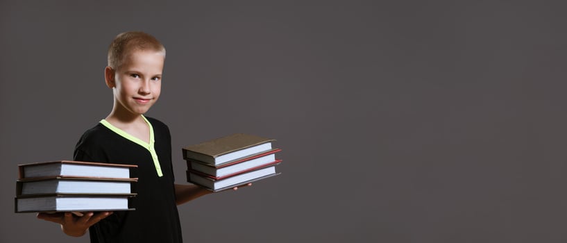 Cute boy holding stacks of books on gray background photo