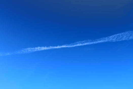 Aircraft condensation contrails in the blue sky inbetween some clouds photo