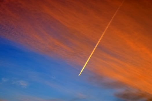 Aircraft condensation contrails in the blue sky inbetween some clouds photo