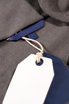 A vertical closeup shot of white blue tags on a string on a cloth with a blank blue tag on the neck photo