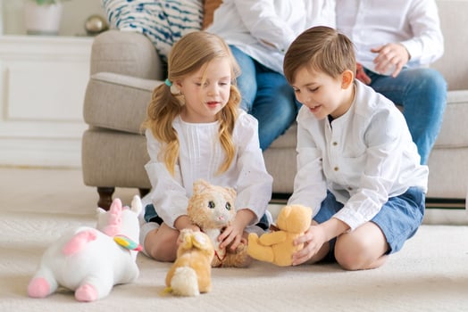 Cute little brother and sister sitting on floor playing with soft toys, parents photo