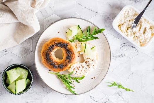 Bagel sandwich with cream cheese, cucumber and arugula on a plate. Homemade breakfast. Top view photo