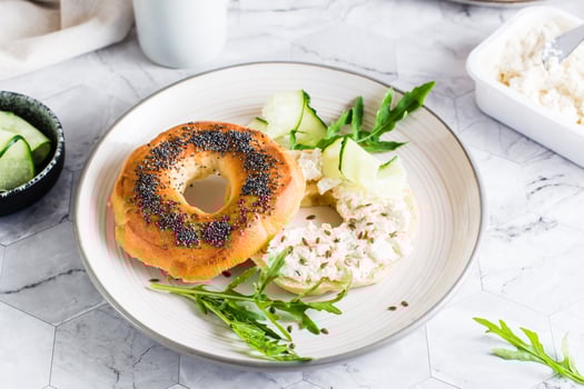 Bagel sandwich with cream cheese, cucumber and arugula on a plate on the table. Homemade breakfast photo