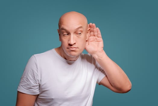 a man on a blue background in holding his hands near his ear, eavesdropping photo