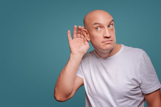 a man on a blue background in holding his hands near his ear, eavesdropping photo
