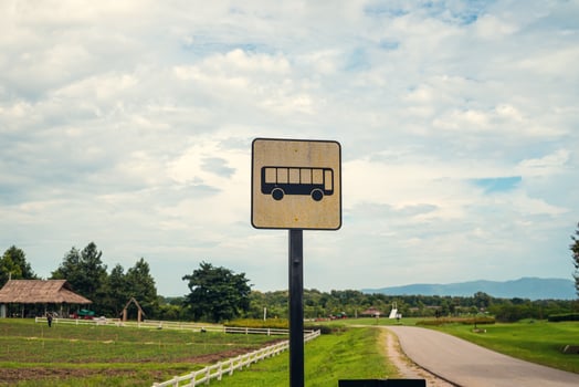 Old fashion bus stop near asphalt country road surrounded by grass green, mountains and farm. Rural nature scene road trip concept and copy space for advertisement. photo