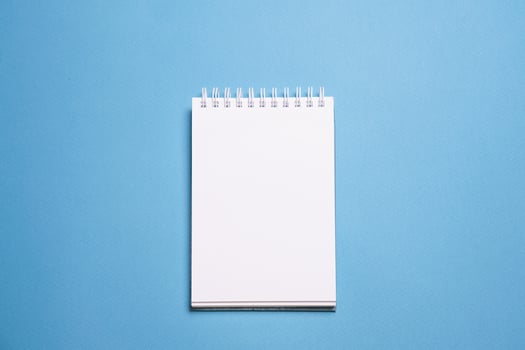 School notebook on blue background, spiral notepad on table, education photo