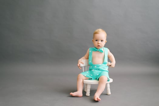 a one-year-old boy is sitting on a white children's chair on a gray background. Copy Space photo