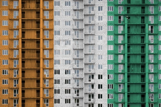 Ivory Coast flag depicted in paint colors on multi-storey residental building under construction. Textured banner on brick wall background photo