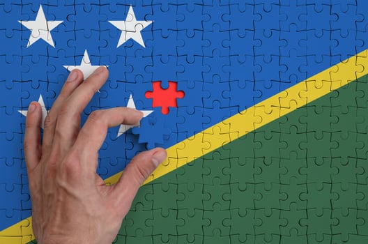 Solomon Islands flag  is depicted on a puzzle, which the man's hand completes to fold photo