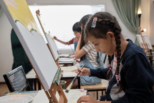 A little girl concentrates on acrylic color picture painting on canvas with multiracial kids in an art classroom, creative learning with talents and skills in the elementary school studio education. photo