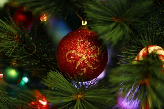 Shiny red Christmas ball on a fir tree with Christmas decorations and blurred lights. photo