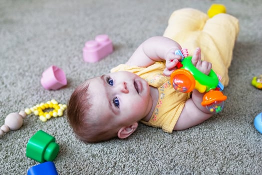 Cute little baby girl lying on a floor and playing with colorful plastic and wooden toys. Develop of child motor skills. photo