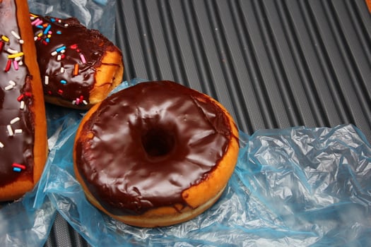 Chocolate donuts and chocolate donut bars topped with multicolored sugar flakes. Placed on a gray aluminum floor. photo