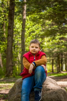 Portrait of a young man in a red tank top in the forest in spring. Walk through the green park in the fresh air. The magical light from the sun's rays falls behind the boy. photo