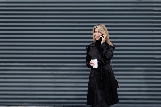 modern businesswoman with a cup of coffee in her hands in business clothes speaks on the phone against the background of a gray textured wall photo