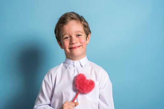 a European boy in a white shirt holds a fluffy red heart in his hands photo