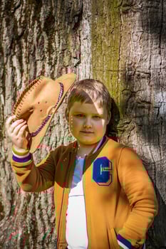 Cute boy posing in a cowboy hat in the woods by a tree. The sun's rays envelop the space. Interaction history for the book. Space for copying photo