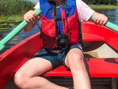 A man in a red boat, shorts and a life jacket is paddling with oars on a boat for a walk on the water of the lake river sea in nature photo