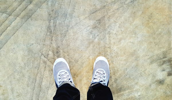 Top view of leg wearing blue jeans and gray or grey sneakers or fashion shoes on floor with car wheel or brake mark on road or street with copy space. Flat lay of part body. Abstract background photo