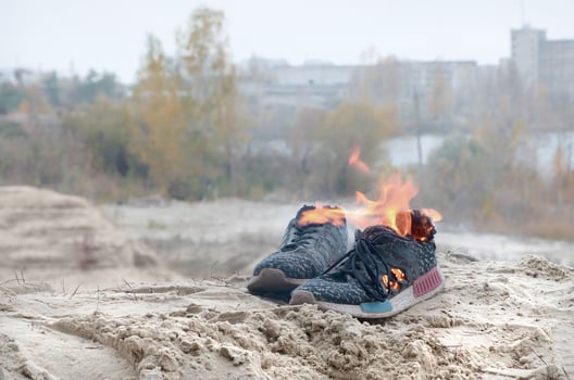 Burning sports sneakers or gym shoes on fire stand on sandy beach coast. Athlete burned out. Physical exertion during training concept photo