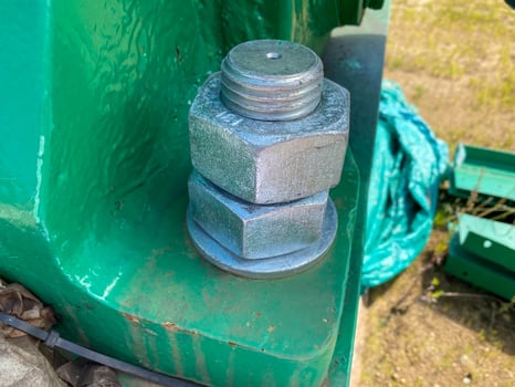 Two nuts are screwed onto a large iron metal stainless mounted threaded bolt. Close view photo