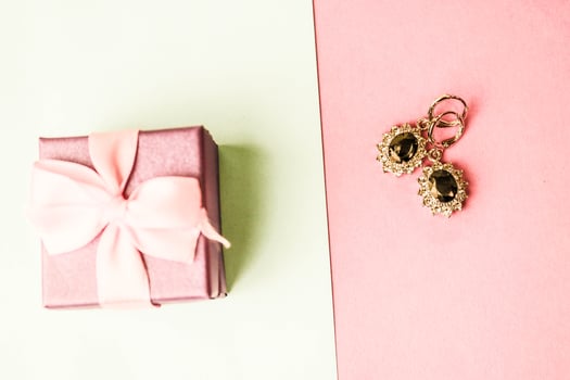 Beauty box, festive beautiful gift box with a bow with silver earrings with precious stones on a pink purple and blue background. Flat lay. Top view photo