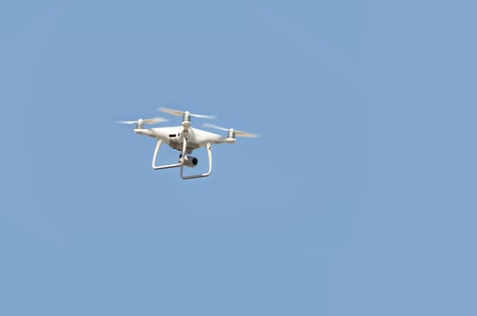 Big white drone hovering in a bright cloudless blue sky photo