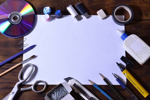 A school or office still life with a white blank sheet of paper and many office supplies. The school supplies lie on a brown wooden background. Place for text photo