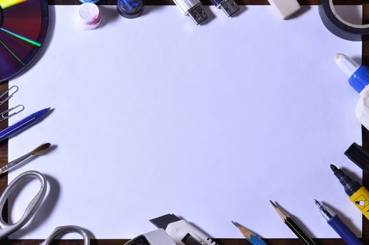 A school or office still life with a white blank sheet of paper and many office supplies. The school supplies lie on a brown wooden background. Place for text photo
