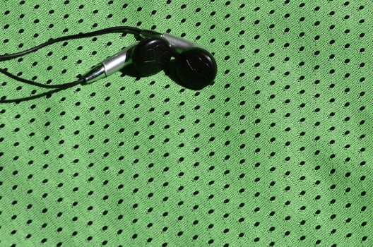 Black earphones lie on the green sportswear of polyester nylon fiber. The concept of listening to music during sports training with modern technology photo