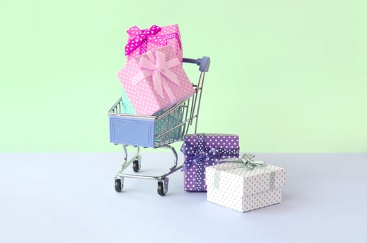 Small gift boxes of different colors with ribbons in shopping cart on a violet and blue pastel background photo