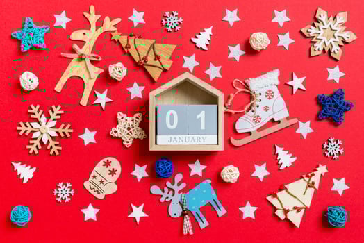 Top view of wooden calendar, holiday toys and decorations on red Christmas background. The first of January. New Year time concept photo