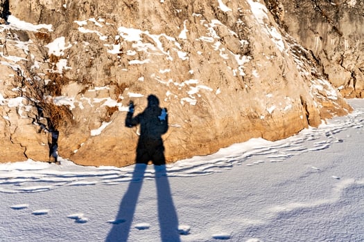 female shadow with long legs and a raised hand on fresh snow and a rock on a winter sunny day. Abstract photo